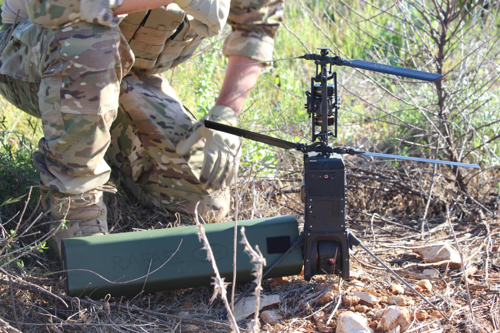 Drone de combate, na cor preta, da Rafael Advanced Systems, utilizado em combates militares em Israel, sendo preparado por um soldado, apoiado no chão.